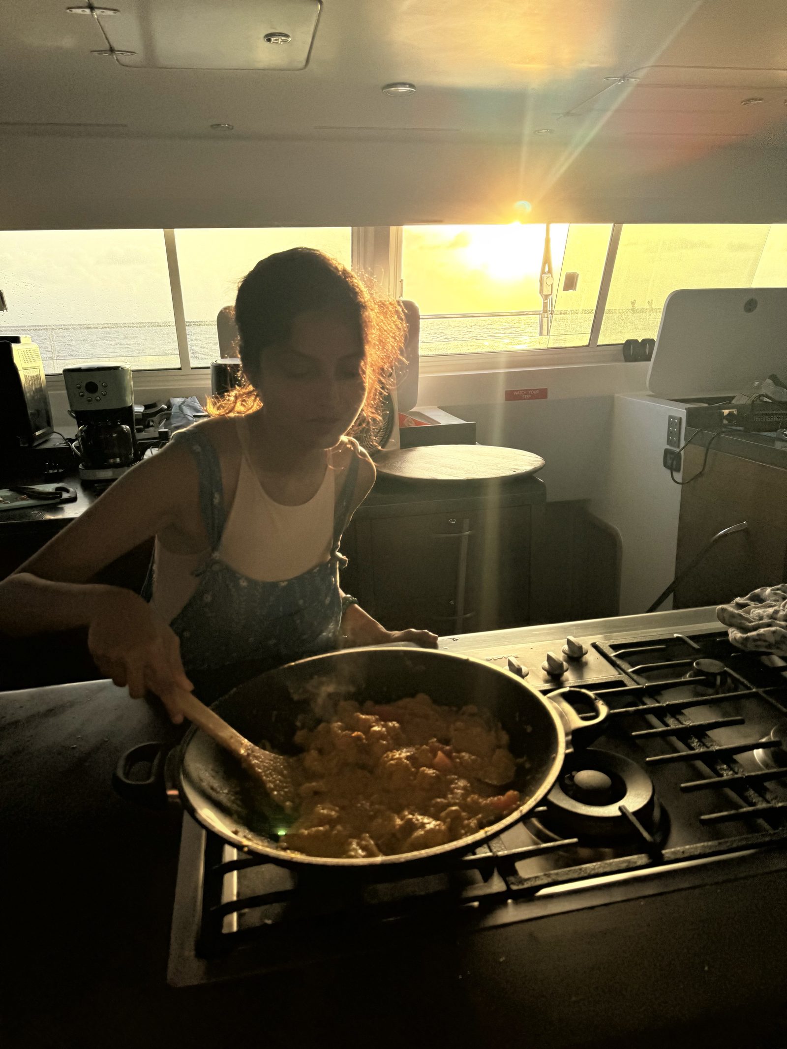 Cooking a curry at the galley stove as sunset light streams through the boat windows.