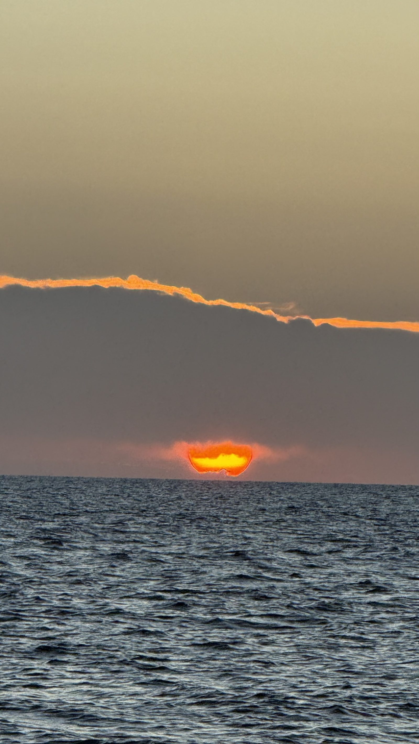 A vivid orange sun sinking into the ocean horizon at sunset, seen from the boat.