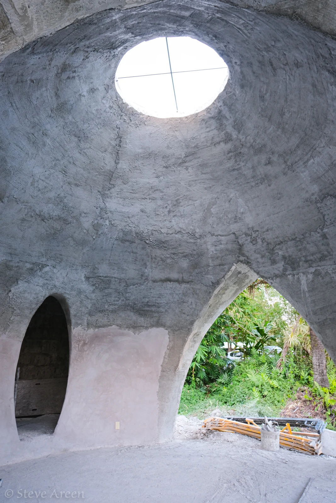 Raw aircrete dome interior with oculus and arched openings.